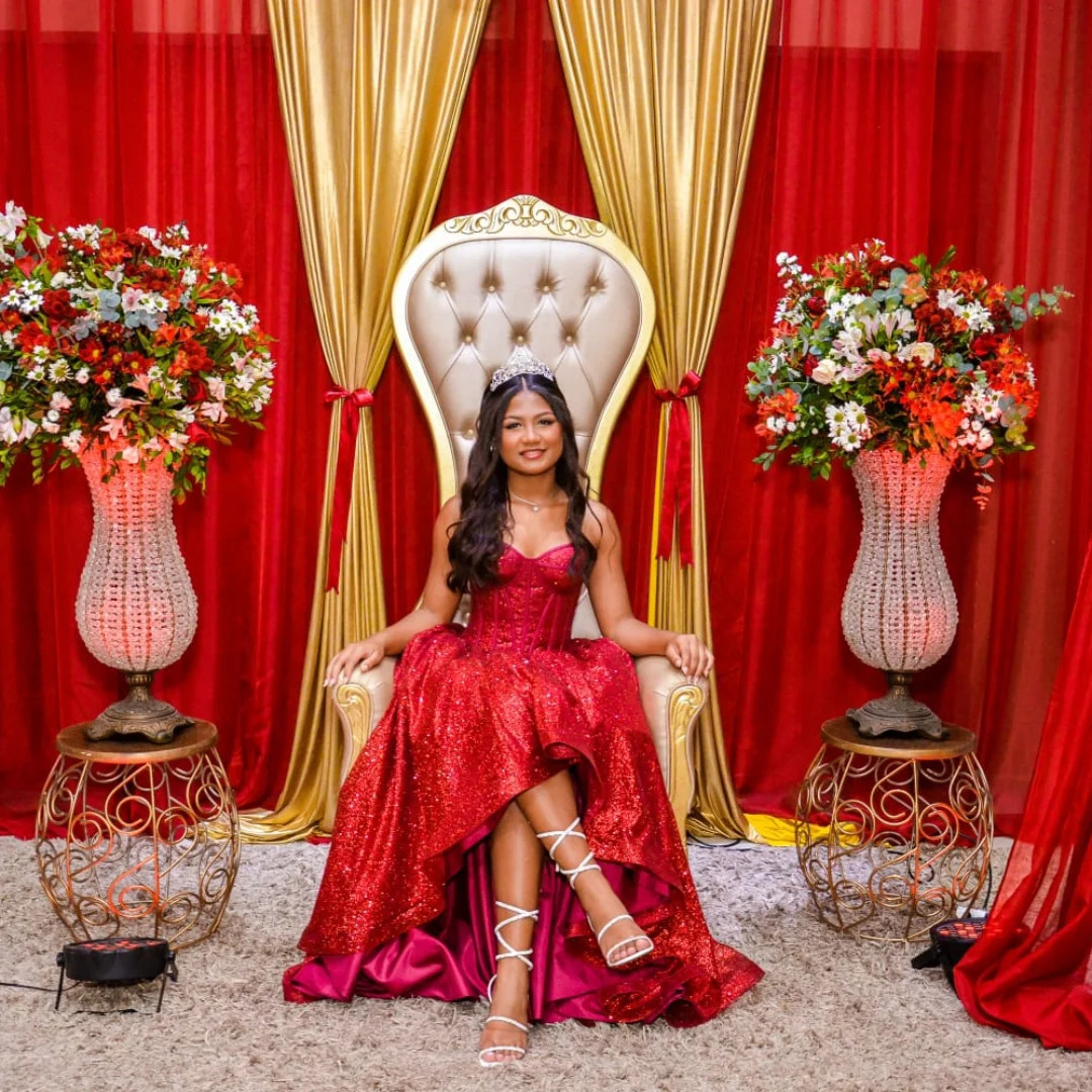 Debutante em trono real com decoração vermelha e dourada