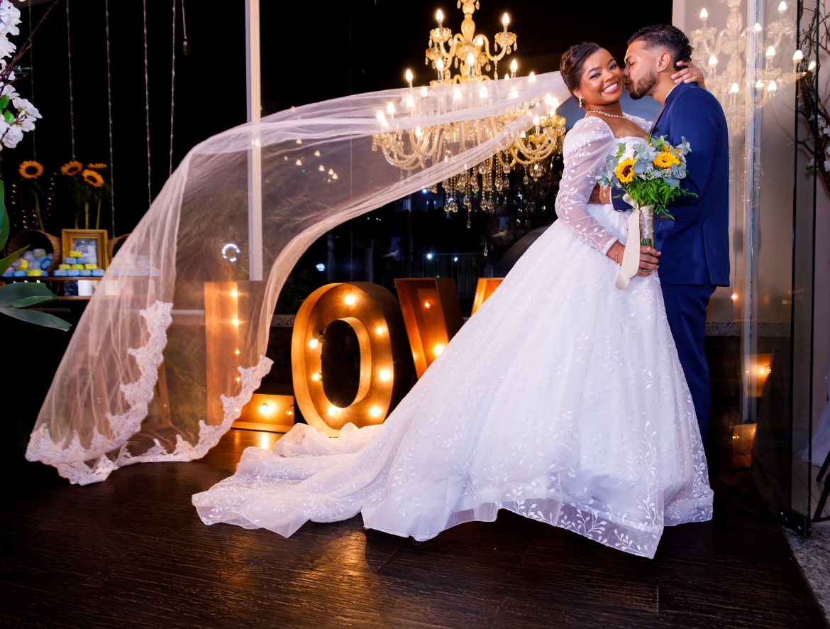 Noivos se beijando com letreiro LOVE e lustre de cristal ao fundo